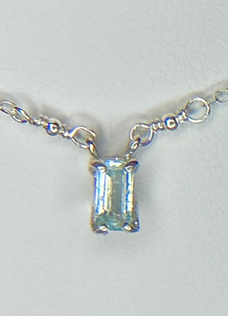 May include: A delicate silver chain necklace with a small, rectangular, light blue gemstone pendant.