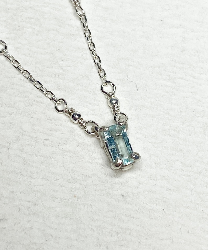 May include: A delicate silver chain necklace with a light blue aquamarine gemstone pendant.