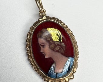 May include: Gold pendant necklace featuring an oval portrait of a woman in profile. The portrait has a red background, a woman with blonde hair and a blue dress. The pendant is framed with a gold filigree border.