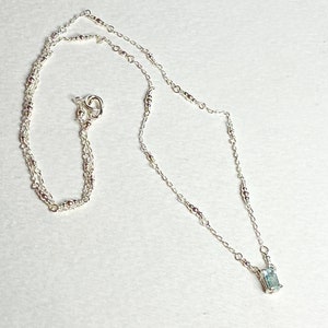 May include: A silver necklace with a delicate chain and a small, rectangular blue gemstone pendant.