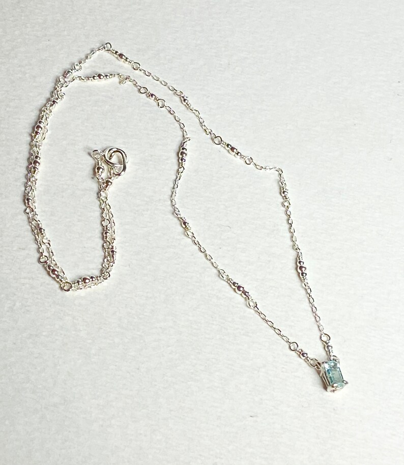 May include: A silver necklace with a delicate chain and a small, rectangular blue gemstone pendant.