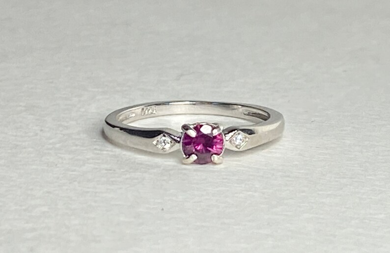 Op de afbeelding: Een zilveren ring met een roze edelsteen en twee kleinere witte edelstenen.