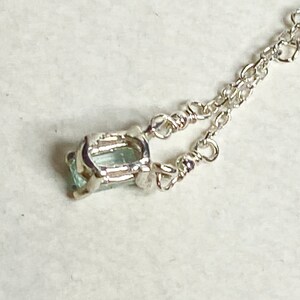 May include: A silver chain necklace with a light blue gemstone pendant. The pendant is set in a silver frame.