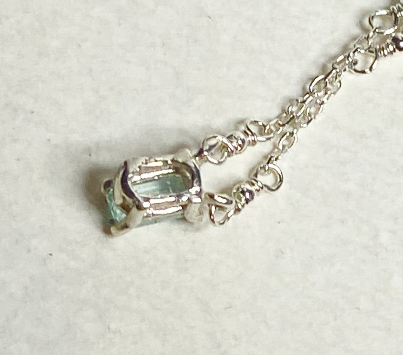 May include: A silver chain necklace with a light blue gemstone pendant. The pendant is set in a silver frame.