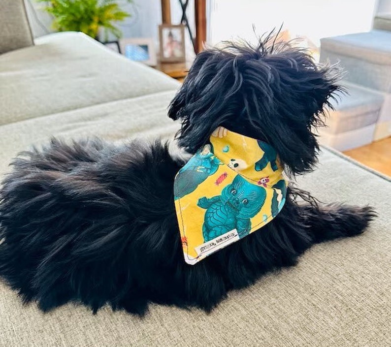 May include: A black dog wearing a yellow bandana with a blue and green cupie doll Swamp Thing monster print.