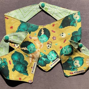 May include: Three yellow fabric bandanas with green and black monster and skull designs. The bandanas have green and white checkered fabric on the back. The bandanas have a button on the top corner.
