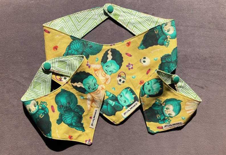 May include: Three yellow fabric bandanas with green and black monster and skull designs. The bandanas have green and white checkered fabric on the back. The bandanas have a button on the top corner.