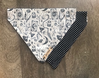 Puede incluir: Bandana para perros con un diseño de cartas del tarot en gris oscuro sobre un fondo beige. El diseño incluye lunas, estrellas y otros elementos celestiales. El reverso es negro con lunares blancos. Una pequeña etiqueta de cuero dice "JoyStar".