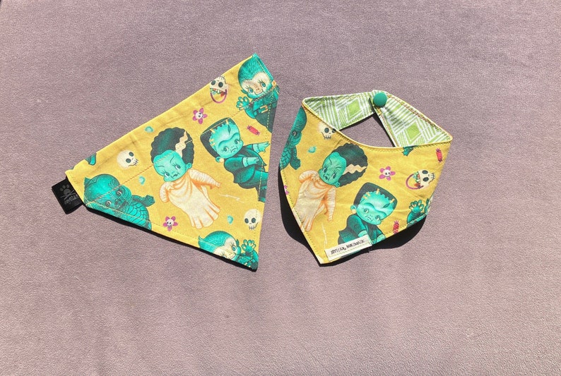 May include: Two yellow fabric bandanas with a green and black monster theme. The bandanas feature a variety of cartoon cupie doll monsters, including Frankenstein, Dracula, and the Creature from the Black Lagoon. The bandanas are both triangular in shape and have a green button on the top corner.