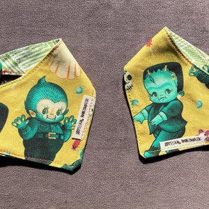 May include: Two triangular fabric bandanas featuring a yellow background with green monster illustrations, including a creature resembling Frankenstein's monster. Each bandana has a green snap button closure and a white tag labeled JAYSSTAR HANDMADE.