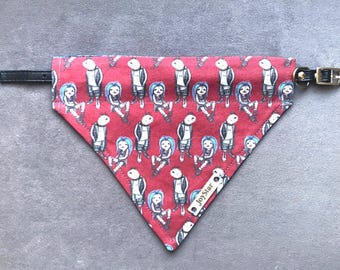 May include: A triangular pet bandana in red fabric featuring a repeating pattern of cartoon characters with blue hair and white outfits. The bandana includes a black leather-like strap with a gold-tone metal buckle and a small metal tag labeled JoyStar.