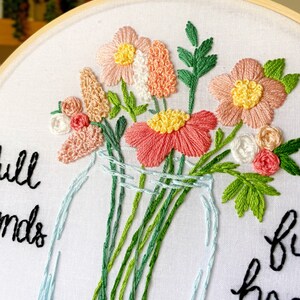 Puede incluir: Arte de bordado en aro con un ramo de flores rosas y blancas en un tarro de vidrio transparente. El texto "Full of Friends" est&aacute; bordado en hilo negro sobre la tela blanca.