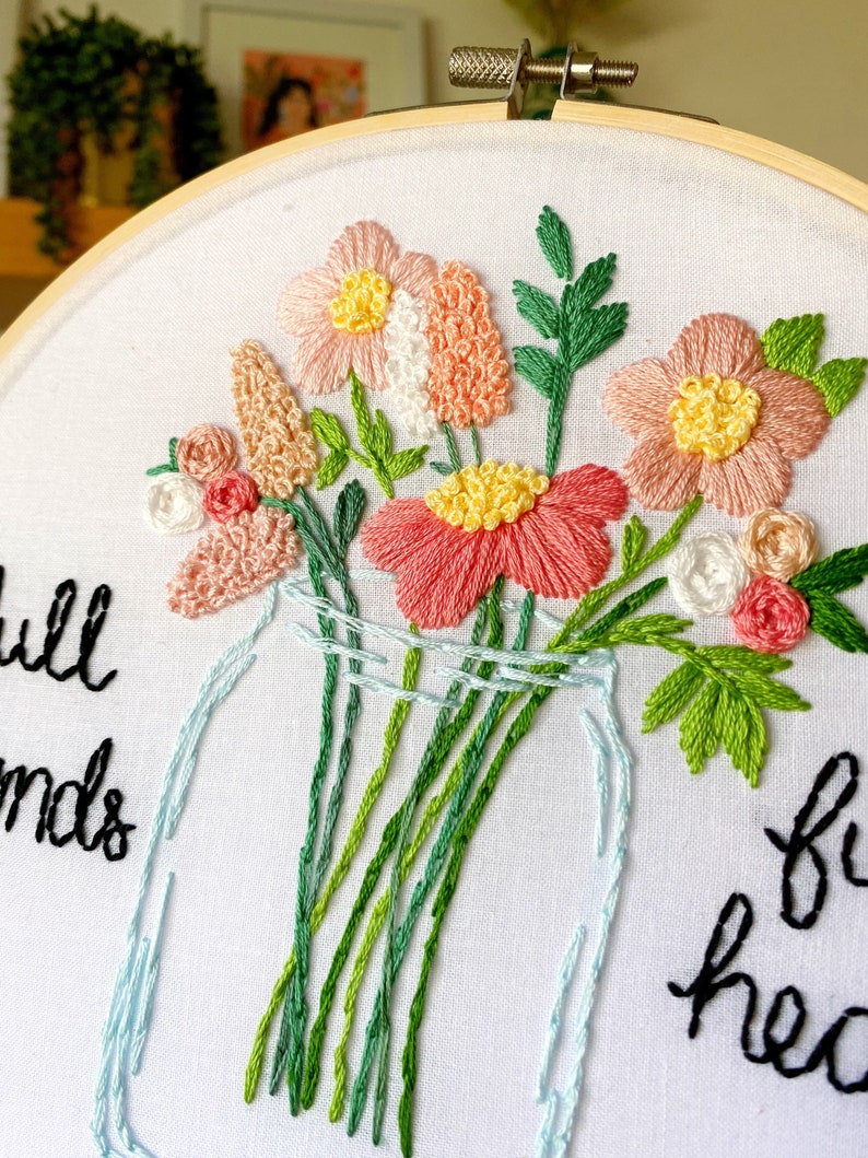 Puede incluir: Arte de bordado en aro con un ramo de flores rosas y blancas en un tarro de vidrio transparente. El texto "Full of Friends" est&aacute; bordado en hilo negro sobre la tela blanca.