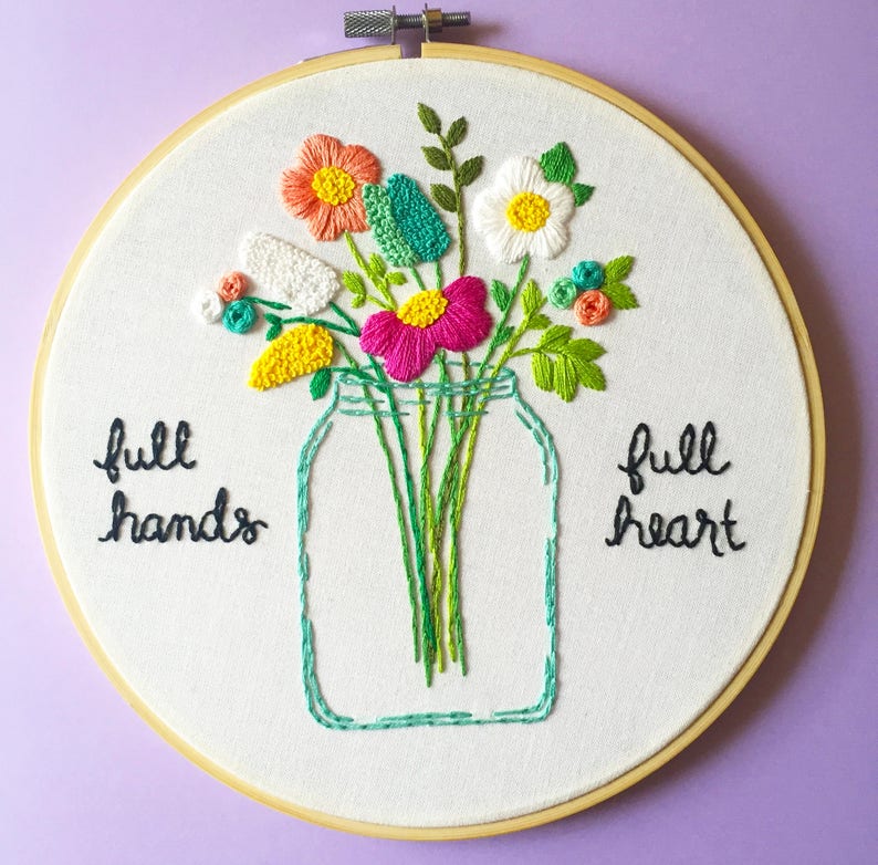 Puede incluir: Arte de bordado en aro con un ramo de flores en un frasco de vidrio. Las flores son rosas, blancas, amarillas y verdes. El texto "full hands full heart" est&aacute; bordado en el aro.