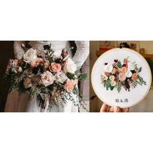 May include: A white embroidery hoop with a floral design in shades of pink, peach, and burgundy. The date "10.6.18" is embroidered in black thread below the flowers.