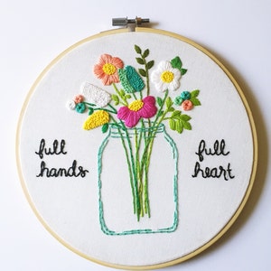 Puede incluir: Arte de bordado en aro con un ramo de flores en un tarro de cristal. Las flores son rosas, blancas, amarillas, verdes y naranjas. El texto "full hands full heart" est&aacute; bordado debajo del tarro.