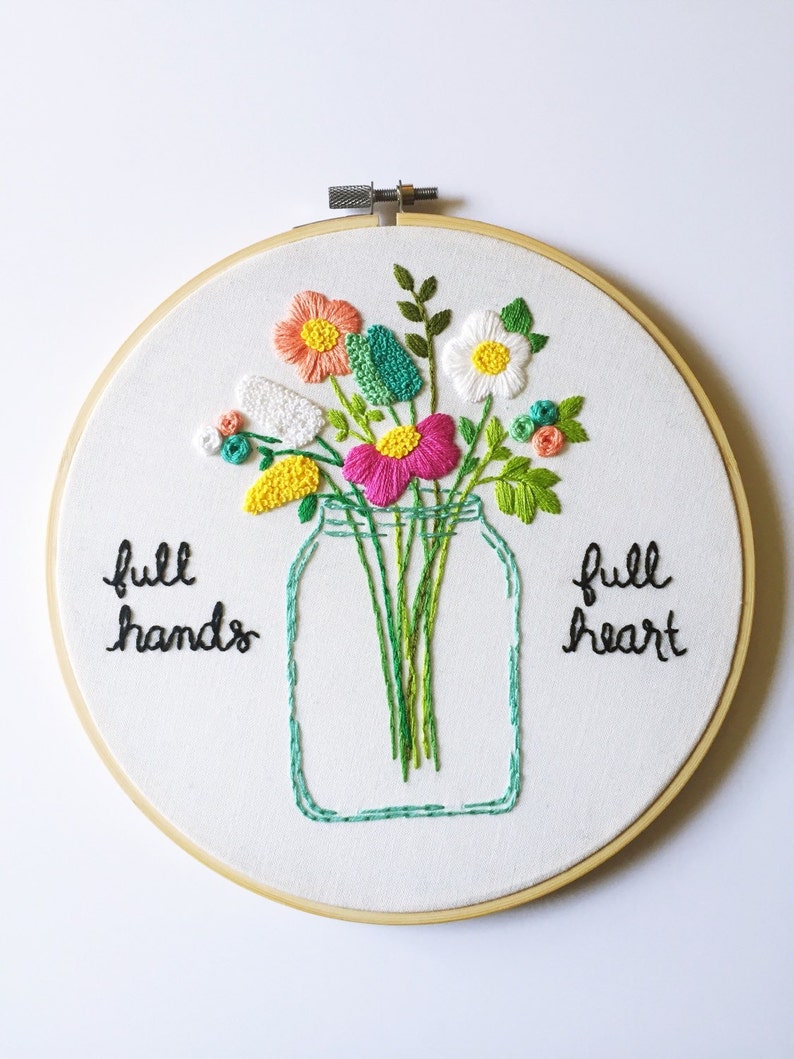 Puede incluir: Arte de bordado en aro con un ramo de flores en un tarro de cristal. Las flores son rosas, blancas, amarillas, verdes y naranjas. El texto "full hands full heart" est&aacute; bordado debajo del tarro.