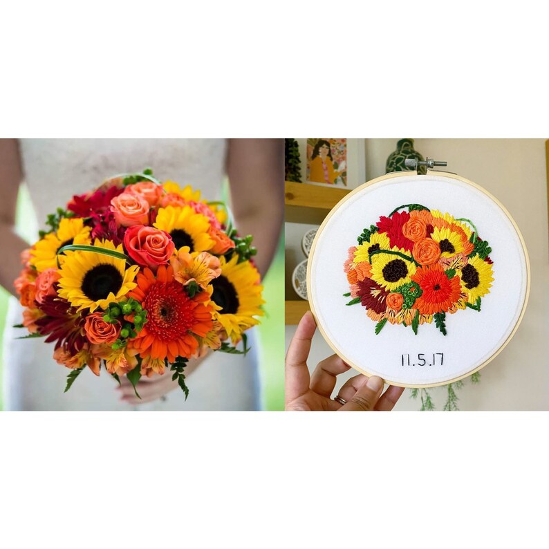 May include: A close-up of a hand holding a circular embroidery hoop with a floral design of sunflowers, orange and red flowers, and green leaves. The embroidery is on white fabric and the date "11.5.17" is stitched in black thread at the bottom.