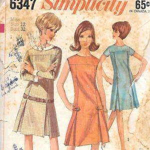 May include: Vintage Simplicity sewing pattern, size 12, bust 32. The illustration shows three dresses: a plaid dress with a belt, an orange dress with buckle details, and a blue dress with pleats. The pattern number is 6347.