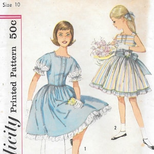 May include: Vintage Simplicity sewing pattern for a girl's dress, size 10. The illustration shows two girls in dresses. One is wearing a light blue dress with white lace trim. The other is wearing a striped dress with a bow.