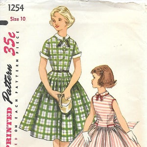 May include: Vintage Simplicity pattern 1254 featuring two dresses. One dress is green plaid with a white collar and cuffs, the other is red and white striped. The pattern details are printed on each piece.