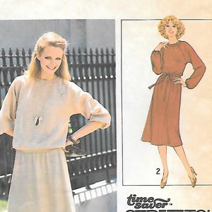 May include: A Simplicity 8678 sewing pattern envelope for a miss dress in size R (14, 16, 18). The cover features a light beige dress with long sleeves and a matching skirt, alongside a brown dress illustration labeled Time Saver Stretch Knit.