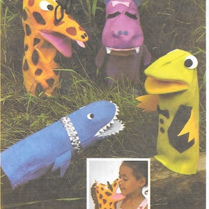 May include: A collection of handmade animal puppets, including a giraffe, hippo, shark, and lizard. The giraffe puppet is yellow with brown spots, the hippo is purple, the shark is blue, and the lizard is green. The puppets are made of fabric and designed for children's play.