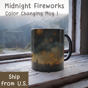 May include: A color-changing mug with a black handle and a design of fireworks over a city skyline. The mug has the text "Midnight Fireworks Color Changing Mug !" in white. The mug is sitting on a white wooden surface.