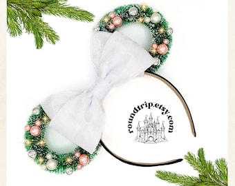 May include: White bow headband with two green wreaths decorated with pink and silver ornaments. The headband has a black band with the text "roundtrip.etsy.com" and a black and white illustration of a castle.