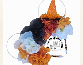 May include: Orange, white, and black flower headband with a witch hat on top. The headband is made of wire and has a castle logo on the side.