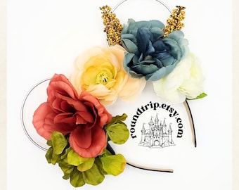 May include: A floral headband with a variety of flowers in shades of red, yellow, blue, and white. The headband is decorated with small green leaves and has a black velvet band. The headband is adorned with a small castle graphic and the text "roundtrip.etsy.com".