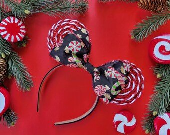 May include: Red and white candy cane patterned headband with a black bow featuring a candy cane and peppermint design. The headband is on a red background.