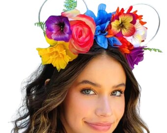 May include: A floral headband with a silver wire frame. The headband features an array of colorful flowers, including yellow, purple, red, and blue blooms. The flowers are arranged across the top of the headband, creating a vibrant and eye-catching accessory.