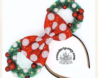 May include: A festive headband featuring a large red sequined bow with white polka dots. The headband has two small green wreaths adorned with red and white ornaments. The text "roundtrip.etsy.com" is visible.