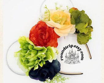 May include: A pair of white mouse ears with a floral arrangement. The flowers are red, orange, green, and black. The ears have a white background with the text "roundtrip.etsy.com" and a black castle graphic.