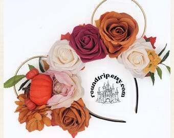 May include: Fall-themed Minnie Mouse ears headband with orange, white, burgundy, and pink roses, a small orange pumpkin, and fall-colored leaves. The headband is black with a gold wire frame. The text "roundtrip.etsy.com" is printed on the headband.
