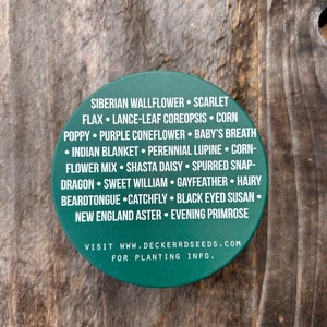 May include: A green round sticker with white text listing a variety of flower seeds. The text reads "Siberian Wallflower, Scarlet Flax, Lance-Leaf Coreopsis, Corn Poppy, Purple Coneflower, Baby's Breath, Indian Blanket, Perennial Lupine, Corn-Flower Mix, Shasta Daisy, Spurred Snap-Dragon, Sweet William, Gayfeather, Hairy Beardtongue, Catchfly, Black Eyed Susan, New England Aster, Evening Primrose. Visit www.deckerrdseeds.com for planting info."