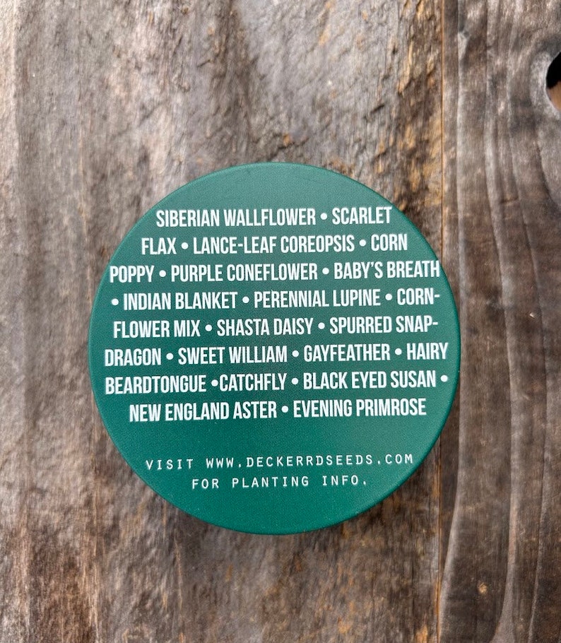 May include: A green round sticker with white text listing a variety of flower seeds. The text reads "Siberian Wallflower, Scarlet Flax, Lance-Leaf Coreopsis, Corn Poppy, Purple Coneflower, Baby's Breath, Indian Blanket, Perennial Lupine, Corn-Flower Mix, Shasta Daisy, Spurred Snap-Dragon, Sweet William, Gayfeather, Hairy Beardtongue, Catchfly, Black Eyed Susan, New England Aster, Evening Primrose. Visit www.deckerrdseeds.com for planting info."