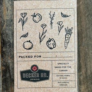 May include: A brown paper card with a black and white illustration of various vegetables and flowers. The card has the text "PACKED FOR" and a logo for "DECKER RD. SEEDS". The text "SPECIALTY SEEDS FOR THE GARDEN ESTABLISHED IN 2012 PHILOMATH, OREGON" is also on the card.