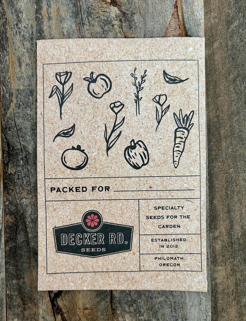 May include: A brown paper card with a black and white illustration of various vegetables and flowers. The card has the text "PACKED FOR" and a logo for "DECKER RD. SEEDS". The text "SPECIALTY SEEDS FOR THE GARDEN ESTABLISHED IN 2012 PHILOMATH, OREGON" is also on the card.