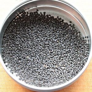 May include: A close-up view of a metal container filled with small, black seeds.