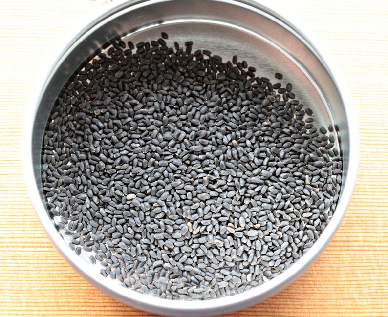 May include: A close-up view of a metal container filled with small, black seeds.