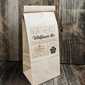 May include: A brown paper bag with a label that reads "Northeast Wildflower Mix" and "flower mix suited for the Northeast". The label also includes the text "Decker Rd. Seeds", "covers 2000 sq. ft.", and "8 oz.".