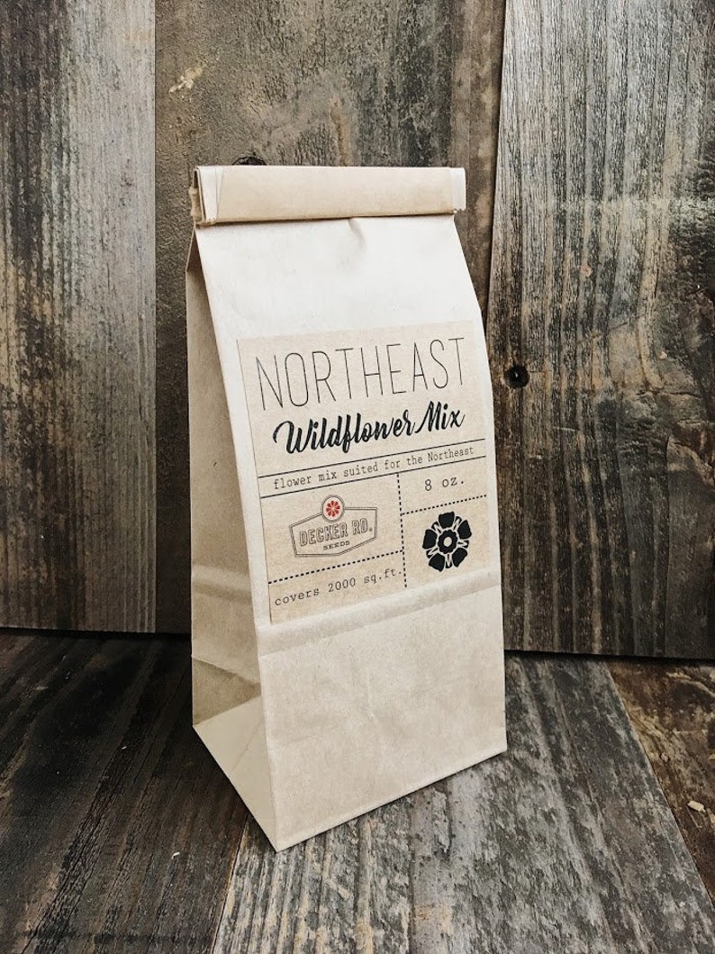 May include: A brown paper bag with a label that reads "Northeast Wildflower Mix" and "flower mix suited for the Northeast". The label also includes the text "Decker Rd. Seeds", "covers 2000 sq. ft.", and "8 oz.".