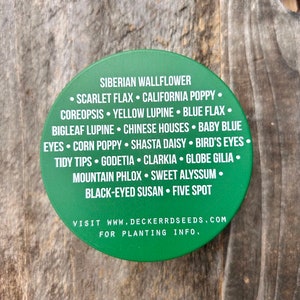 May include: Green round sticker with a white border and white text listing a variety of flower seeds. The text reads "Siberian Wallflower, Scarlet Flax, California Poppy, Coreopsis, Yellow Lupine, Blue Flax, Bigleaf Lupine, Chinese Houses, Baby Blue Eyes, Corn Poppy, Shasta Daisy, Bird's Eyes, Tidy Tips, Godetia, Clarkia, Globe Gilia, Mountain Phlox, Sweet Alyssum, Black-Eyed Susan, Five Spot". The text also includes "Visit www.deckerrdseeds.com for planting info."
