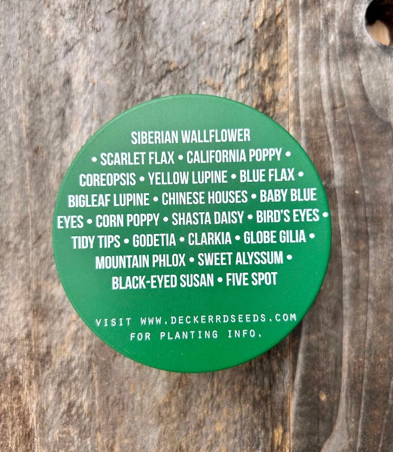 May include: Green round sticker with a white border and white text listing a variety of flower seeds. The text reads "Siberian Wallflower, Scarlet Flax, California Poppy, Coreopsis, Yellow Lupine, Blue Flax, Bigleaf Lupine, Chinese Houses, Baby Blue Eyes, Corn Poppy, Shasta Daisy, Bird's Eyes, Tidy Tips, Godetia, Clarkia, Globe Gilia, Mountain Phlox, Sweet Alyssum, Black-Eyed Susan, Five Spot". The text also includes "Visit www.deckerrdseeds.com for planting info."