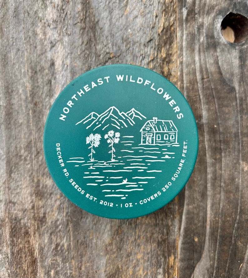 May include: A green round tin with white text and a line drawing of a house, mountains, and flowers. The text reads "Northeast Wildflowers Decker Rd. Seeds Est. 2012 - 1 oz. Covers 250 Square Feet."