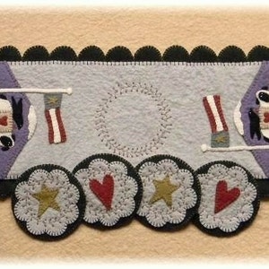 May include: A felt table runner with a patriotic theme. It features two sheep with hearts, two flags, and a wreath. The runner is decorated with four round felt appliques with stars and hearts.