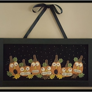 Puede incluir: Una pared de fieltro enmarcada con un fondo negro y una fila de ocho calabazas naranjas con hojas verdes y ojos y bocas negros. Las calabazas est&aacute;n dispuestas en una fila y tienen un fondo de cielo estrellado.