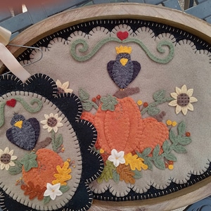 Könnte beinhalten: Zwei Filz-Wandbehänge mit Herbst-Motiv. Der größere zeigt einen schwarzen Vogel mit Krone, Kürbisse und Blätter. Der kleinere zeigt einen schwarzen Vogel, Kürbisse und Blätter. Beide Behänge haben einen gewellten Rand.